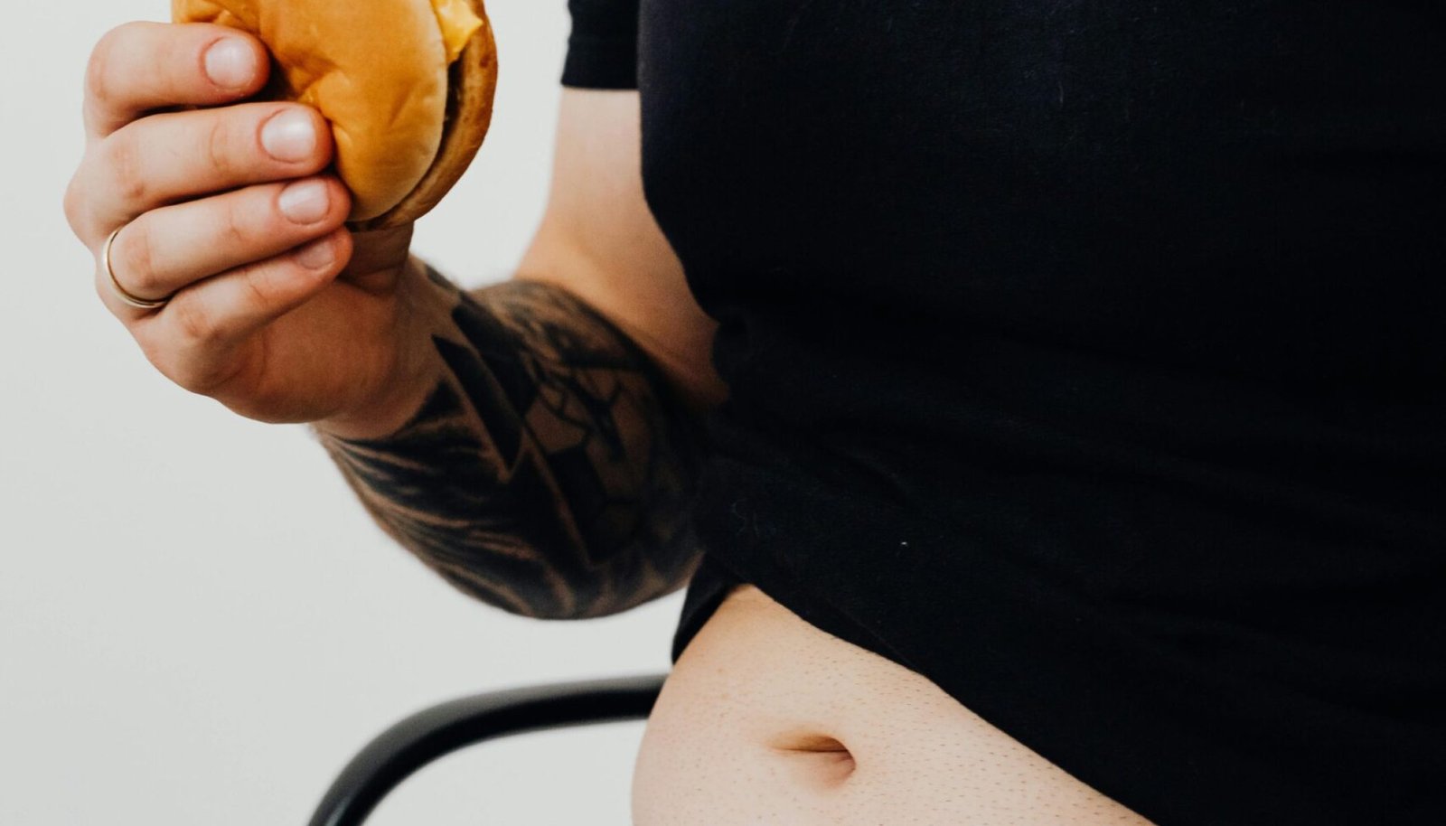 Man wearing black shirt sits holding a burger, highlighting casual eating habits.