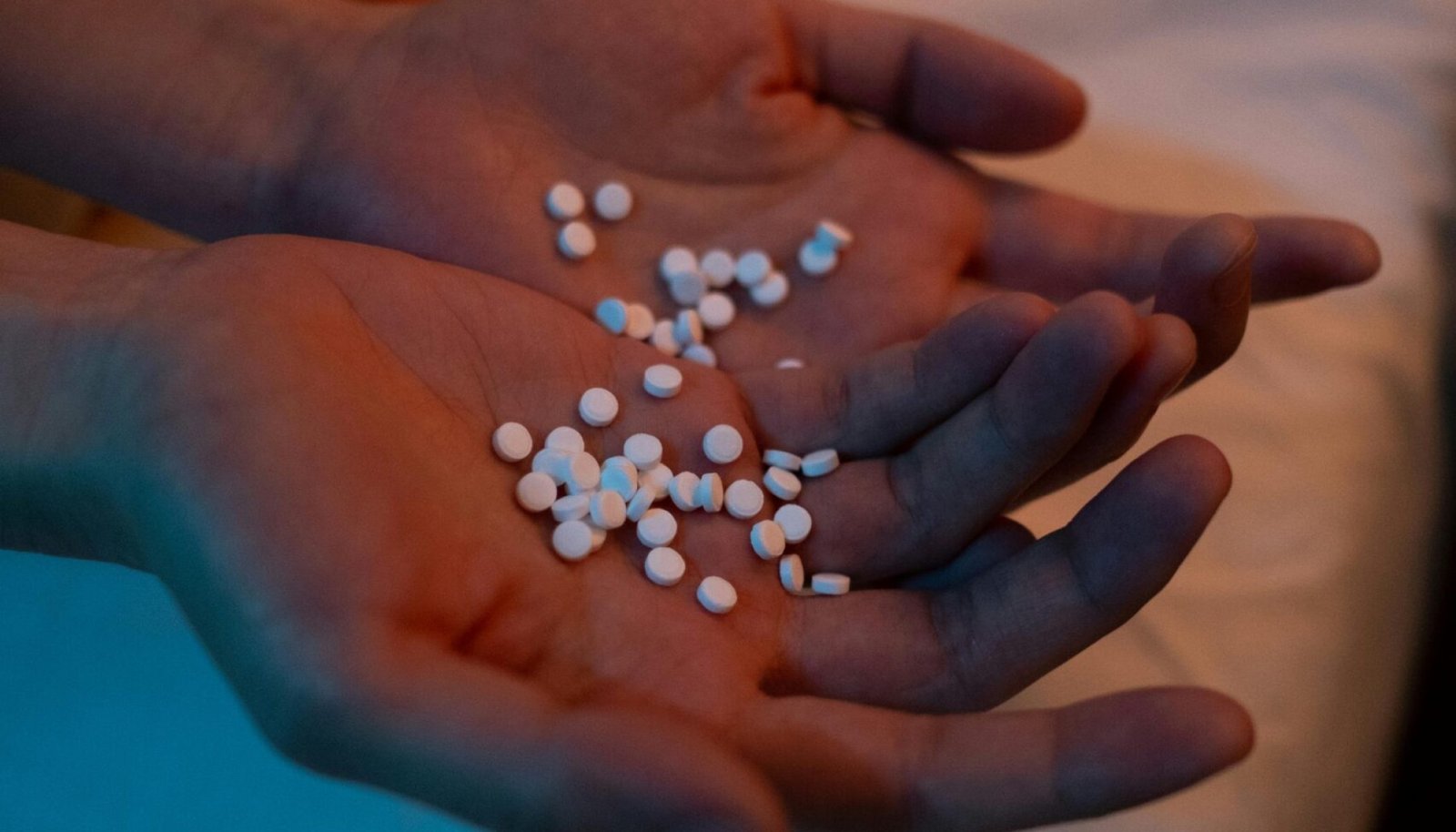 A person holding a handful of pills in a dimly lit bedroom, conveying themes of health and mental wellness.